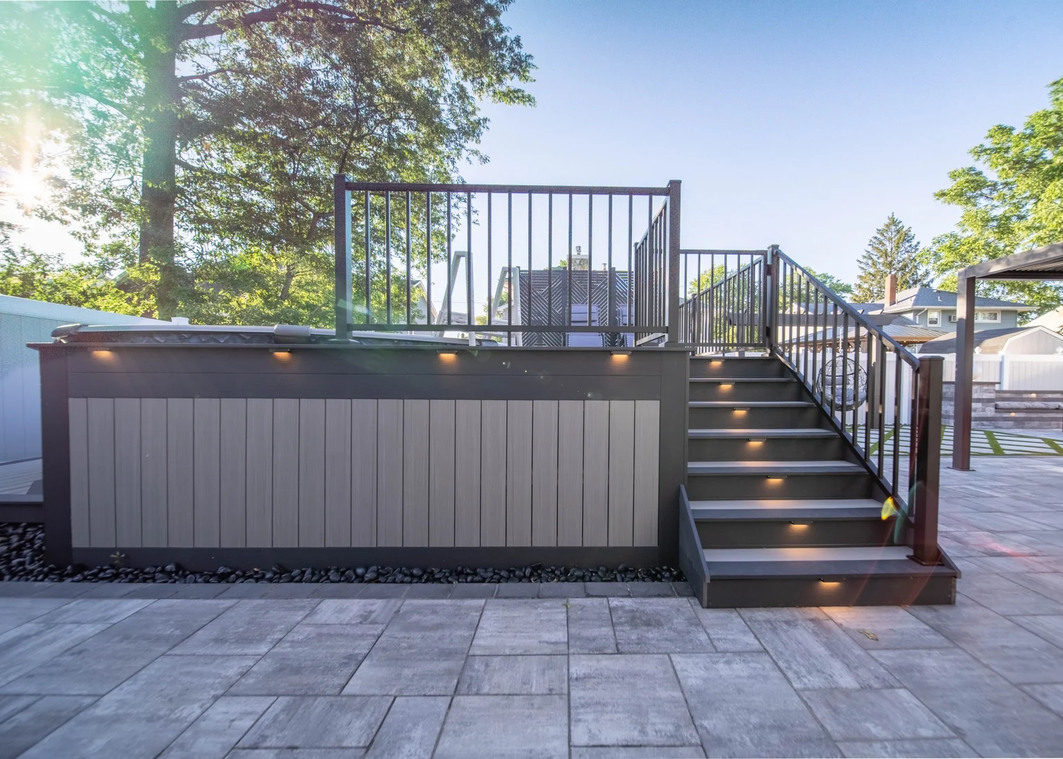 Warm lighting along the deck fascia and staircase, with grey skirting and black railings.