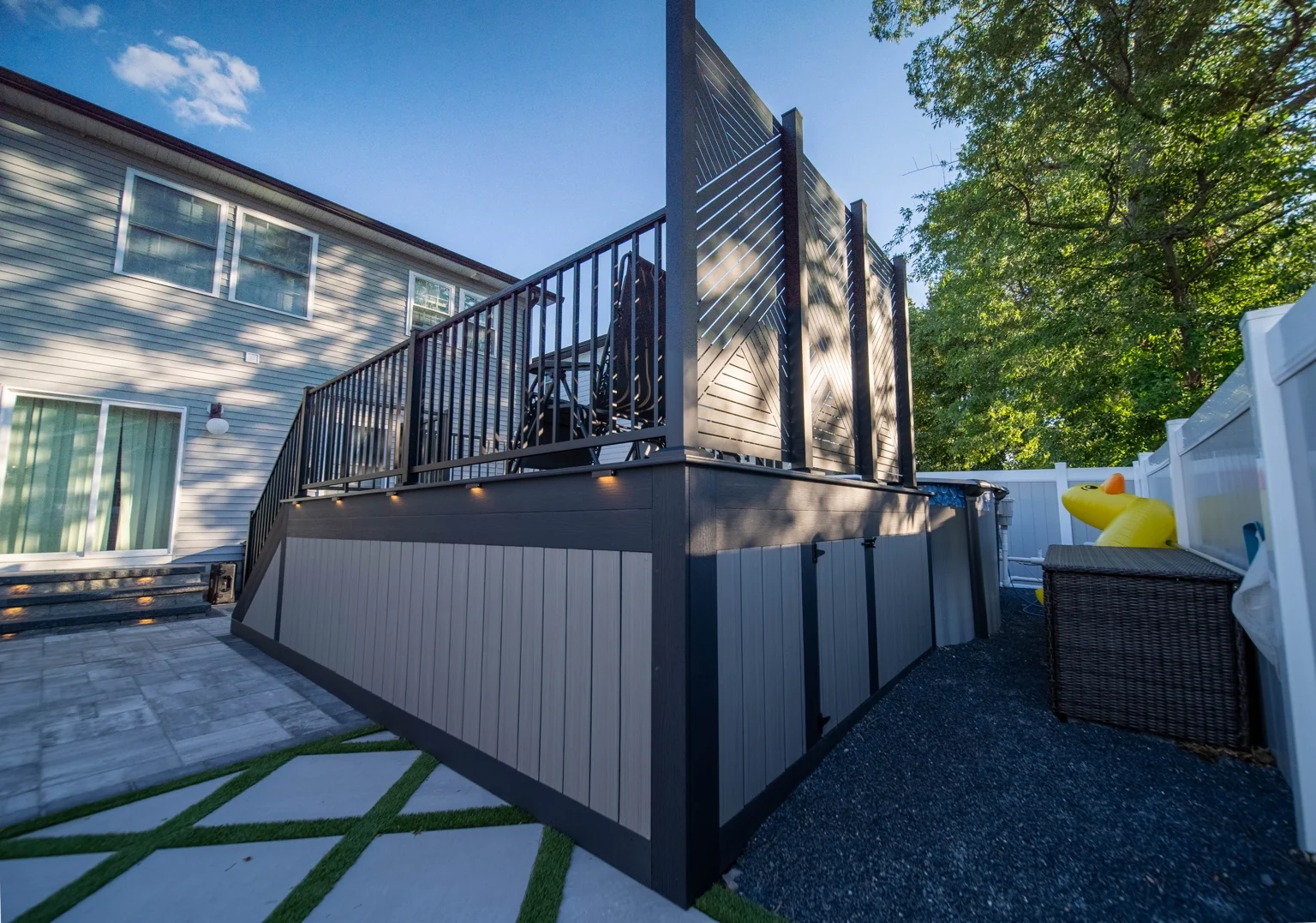 Grey vertical skirting with dark trim, black railings and a tall privacy screen at the deck corner.