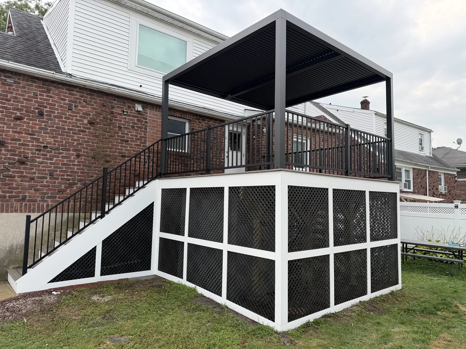 A raised deck with a black pergola, black railings and white-framed lattice skirting.
