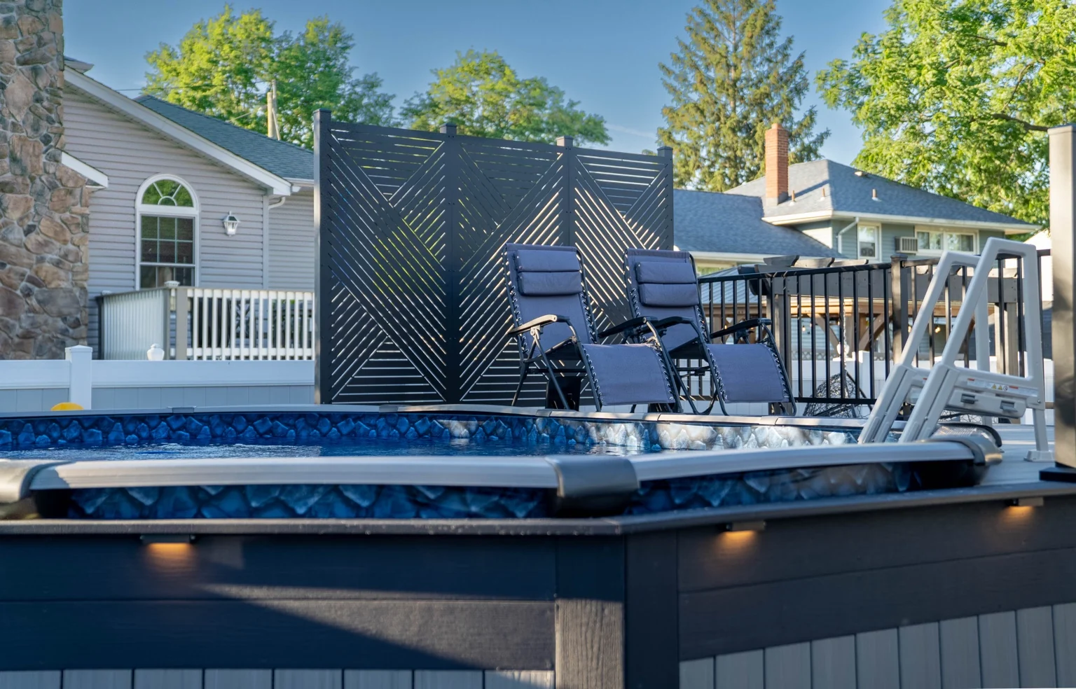 A finished pool deck with lounge chairs, a dark privacy screen and white railings.