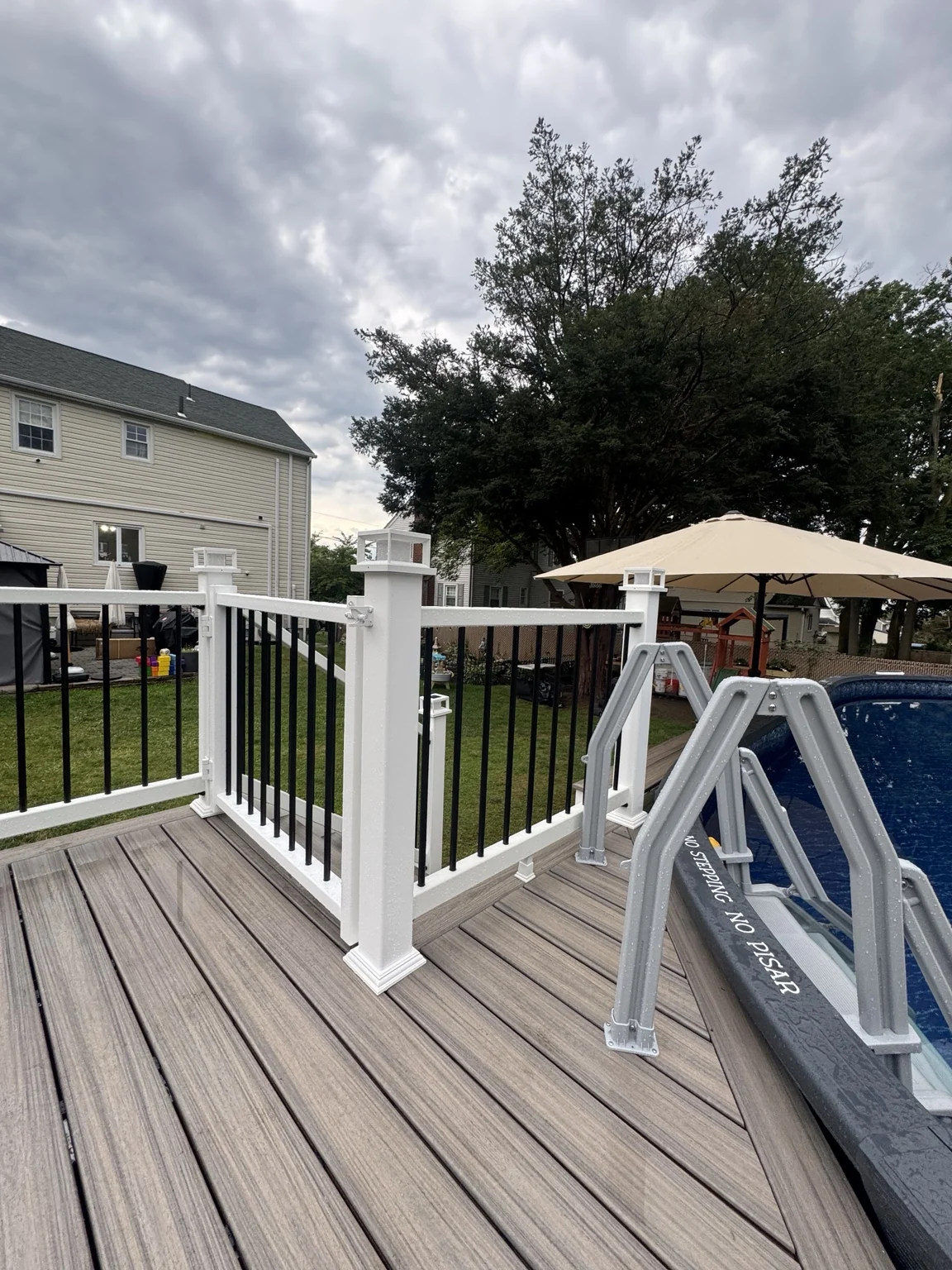 White posts and black balusters frame the deck beside the pool and its access ladder.