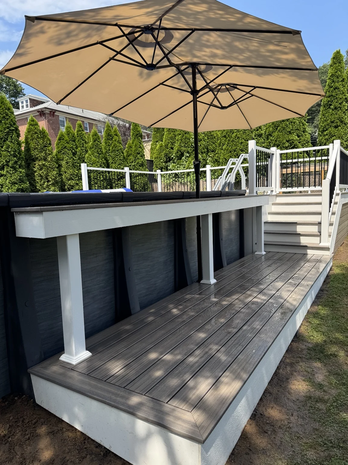 A long poolside bar and lower deck platform with white trim and umbrella shade.