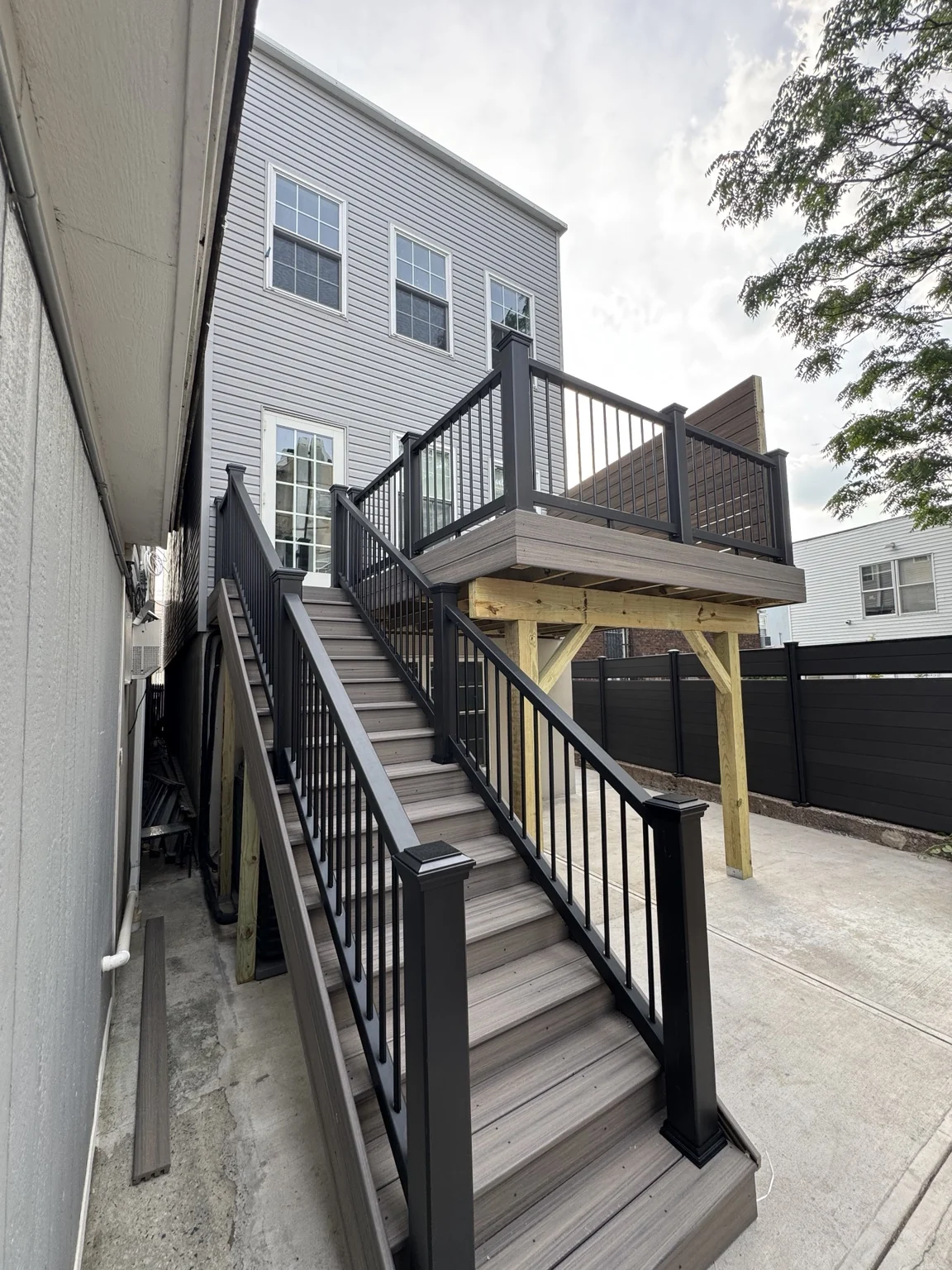 A long staircase with black railings connects the raised deck to the yard below.