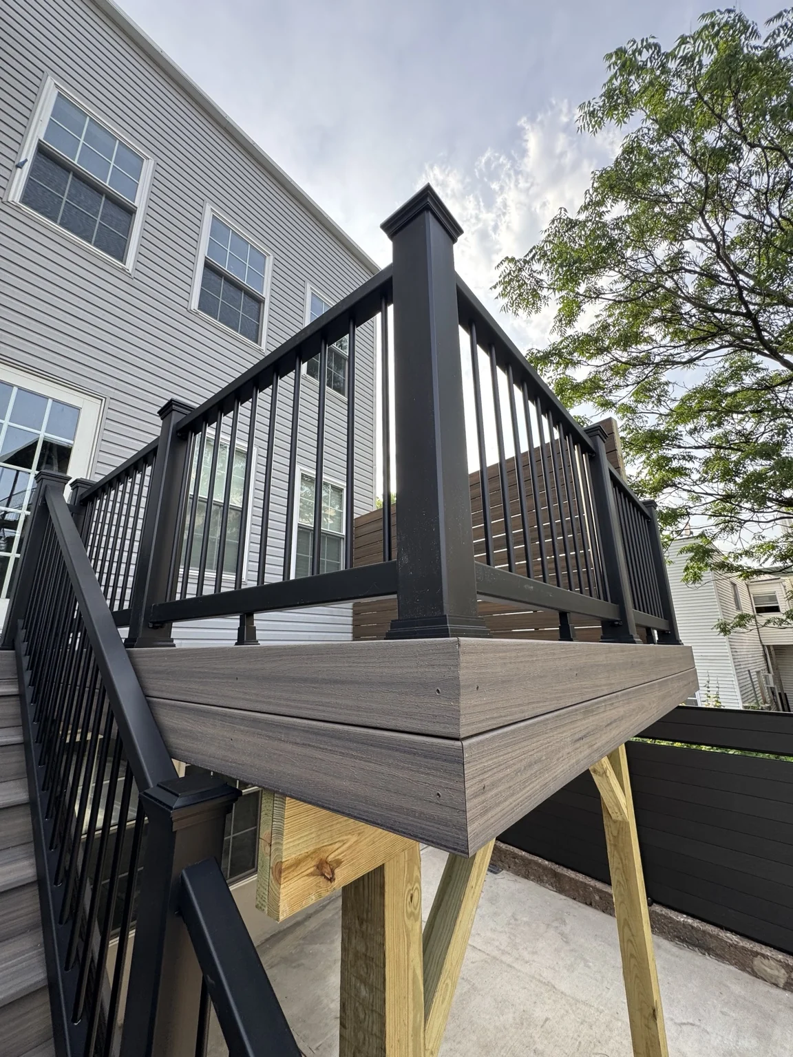 A close view of the raised deck corner, grey fascia, black railings and exposed timber supports.