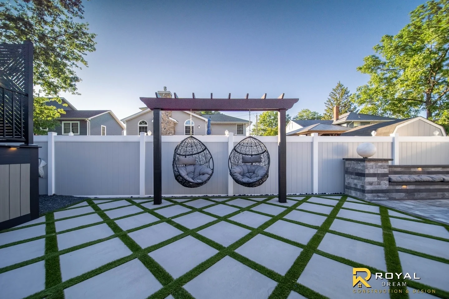 Twin hanging chairs overlook a geometric paver-and-turf courtyard.