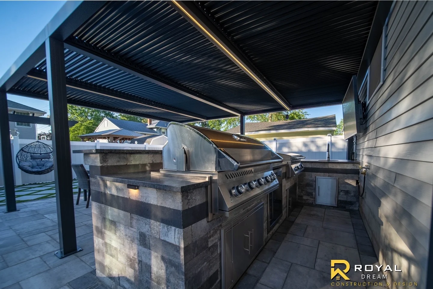 A built-in grill and masonry kitchen beneath the pergola.